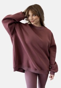 Przytulny, dużych rozmiarów bordowy sweatshirt z prążkowanym dekoltem, opuszczonymi ramionami i długimi rękawami, zestawiony z dopasowanymi prążkowanymi legginsami. Gładka tekstura.