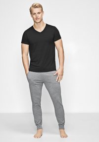 Sort v-neck t-shirt parret med lysegrå sweatpants, der har en slim fit og ribbede manchetter, står foran en ensfarvet hvid baggrund.
