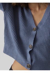 Blå kort cardigan med V-ringning, strukturstickad och tre bruna knappar fram. Har lösa ärmar och ribbat avslut.