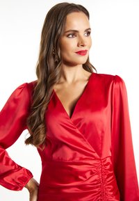 Rochie din satin roșu, cu un decolteu adânc în V, sleevuri lungi și detaliu plisat la talie. Textură netedă cu o siluetă aderentă.