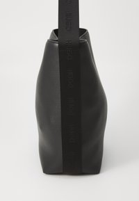 Borsa in pelle nera con una forma triangolare, caratterizzata da una superficie testurizzata e una tracolla in tessuto nero stampata con "HUGO."