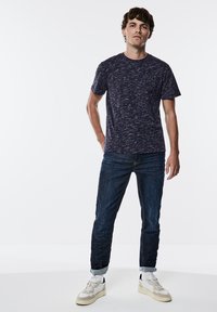 Mörkblå t-shirt med kort ärm och en strukturerad, fläckig mönstring, kombinerad med mörkblå jeans och vita sneakers med beige detaljer.