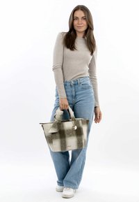 Beige og grøn ternet tote bag med en tekstureret finish, stofsløjfe som accent og et rundt metalcharms fastgjort til håndtaget.
