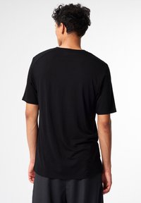 Schwarzes Kurzarm-T-Shirt mit entspannter Passform. Weicher Stoff und minimales Design, mit flachem Ausschnitt und glatten Nähten.