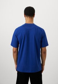 Rövid ujjú, kerek nyakú póló élénk kék színben. Simább textúrával és egyenes aljjal rendelkezik, finom hátvarrás részletezéssel.