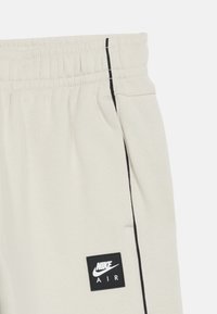 Detalj av off-white Nike Air joggebukser som viser midjebånd, sidelomme, svart sideststripe og svart Nike Air-logo på låret.
