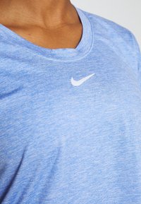 Ljusblå atletisk T-shirt tillverkad av strukturerad väv, med V-ringning och en liten vit Nike-logotyp på bröstet.