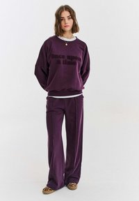 Fialová mikina s textem "bylo nebylo", spárovaná s odpovídajícími širokými kalhotami. Měkký materiál s uvolněným střihem.