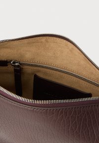 Læderclutch i mørk bordeaux med en tekstureret overflade. Indvendigt har den en glat beige foring, lynlåslomme og kortholder.