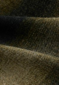 Wollstoff in Erdtönen mit einer strukturierten Oberfläche in verschiedenen Grüntönen und Brauntönen, die ein weiches, flauschiges Erscheinungsbild zeigt.