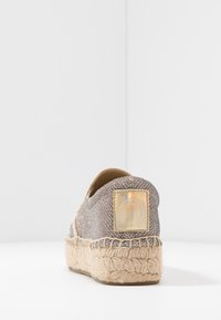 Espadrille schoen met een metallic geweven bovenwerk, beige jute zool, en een vierkante label met een holografische afwerking op de hak.