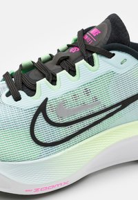 Scarpa da corsa Nike ZoomX in mesh verde chiaro e blu, con lacci neri, swoosh grigio e accento rosa sulla suola. Presenta un design testurizzato.