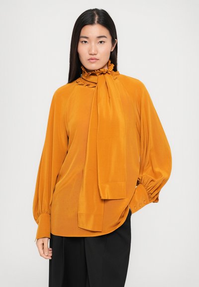Verbrande oranje blouse met een gerimpelde kraag en strikdetail, voorzien van lange mouwen met geplooide manchetten en een zachte, gladde textuur.