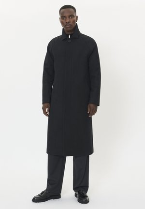 Langer schwarzer Übermantel aus einem glatten Stoff, mit stehem Kragen, vorderem Knopfverschluss und seitlichen Taschen. Taillierte Passform mit gerader Silhouette.