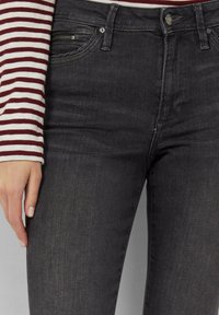 Jean en denim noir avec une coupe slim, présentant un détail de poche zippée et un léger délavage, accompagné d'une chemise à rayures à manches longues.