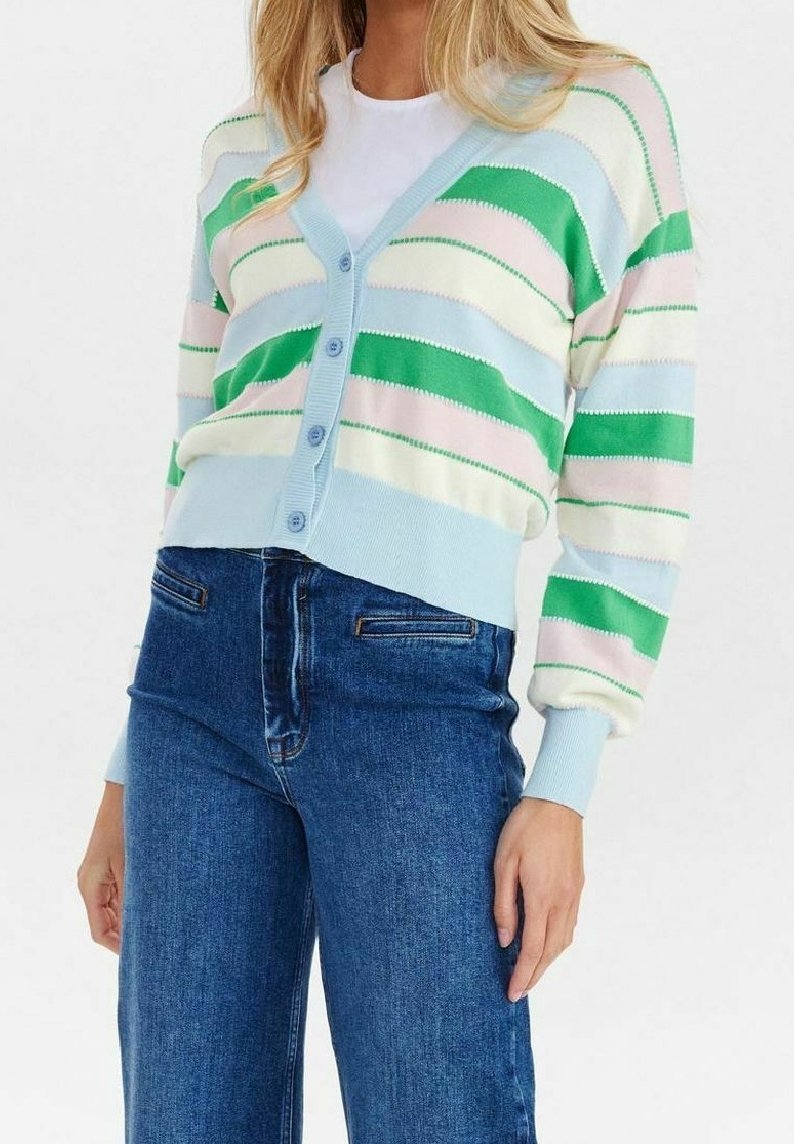 Kvinna som bär en kortärmad cardigan med blå, grön, vit och rosa horisontella ränder över en vit skjorta och högmidjade blå jeans.