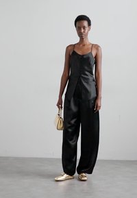 Black satin top with buttons, paired with wide-leg black satin pants. Gold shoes and a small beige handbag complete the outfit.