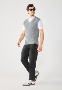 Grå strikket vest med V-hals, lagt over en hvit t-skjorte. Kombinert med svarte bukser og hvite joggesko med svarte striper.