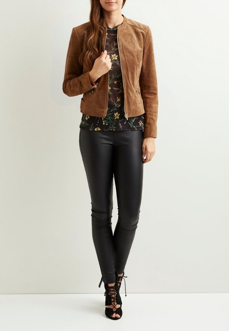 Chaqueta de ante marrón con un diseño ajustado, combinada con una blusa de estampado floral, pantalones de cuero negros y sandalias negras de tacón con cordones.