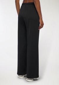 Czarne, szerokie spodnie sportowe o miękkiej fakturze, z elastycznym pasem w talii, zestawione z białymi butami sportowymi. Skoncentrowane na komforcie i swobodzie ruchów.