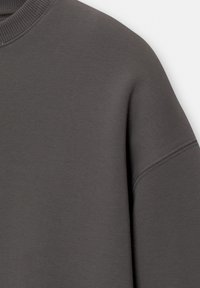 Gros plan d'un sweat-shirt en tissu gris foncé montrant l'épaule, la couture de la manche et le bord côtelé de l'encolure.