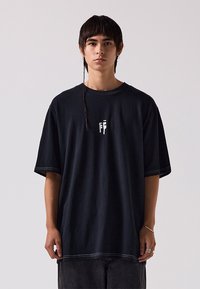 Black oversized cotton t-shirt with short sleeves, featuring a white graphic in the center and contrasting stitching along the seams.