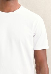 Tricou alb cu mânecă scurtă și guler rotund. Material neted, ușor, cu un design ajustat, având cusături curate și fără logo-uri vizibile.