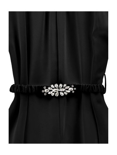 Vestido negro de tela con cintura fruncida y una franja decorativa que presenta un adorno plateado similar a una joya.