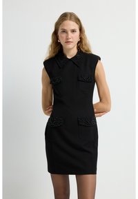 Schwarzes ärmelloses Kleid mit einem Kragen, das auf der Vorderseite mit Perlen verziert ist und eine taillierte Silhouette hat. Glatte Stofftextur.