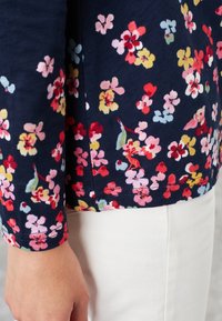 Långärmad skjorta med blommönster i marinblått med rosa, röd, gul och blå blommor. Har en figursydd design och en fyrkantig tygtextur.