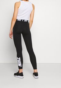 Black leggings with "NIKE" logo printed in white on the lower leg, paired with a white sleeveless top and black athletic shoes.