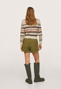 Maglione lavorato a maglia con motivi crema, marrone scuro e rosa; pantaloni corti imbottiti verde oliva; alti stivali di gomma verdi. Vista posteriore, sfondo neutro.