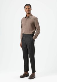 Bruin shirt met lange mouwen en knopen, gecombineerd met donkergrijze, op maat gemaakte broek. Bruine loafers maken de look af. Gladde stof en gestructureerde pasvorm.
