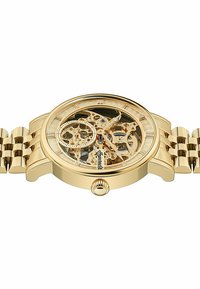 Montre squelette dorée avec un cadran transparent, mécaniques complexes visibles, et un bracelet en métal ton or présentant un design à maillons.