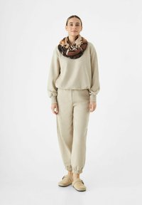 Sweatshirt en polaire beige et pantalons avec des poignets élastiques, associés à une écharpe à motifs multicolores et des chaussures slip-on beiges.