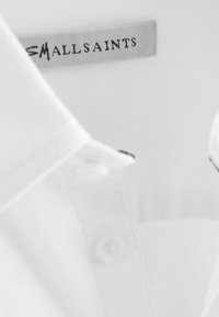 Witte shirt met kraag en knoopdetails, met een gladde textuur en een label met de tekst "MALSAINTS" in zwart op een grijze achtergrond.