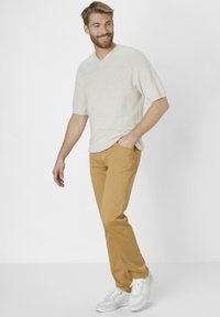 Tan cotton pants paired with a cream short-sleeve, V-neck sweater, and white sneakers. The outfit features a relaxed fit and a subtle texture.