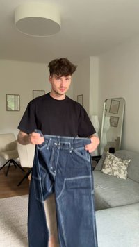 Jeans de ganga azul-escuro, segurados, com costura em contraste, múltiplos bolsos e um corte relaxado. Textura suave e tecido resistente.