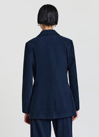 Blazer in corduroy blu navy con rever a scatto, vestibilità slim e spacchetto singolo sul retro. Superficie texture con un sottile motivo a coste.