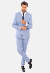 Abito azzurro chiaro con tessuto testurizzato, design a un solo petto, camicia bianca e cravatta blu navy; scarpe nere lucide; in posa in piedi.