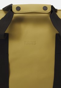Olíva zöld RAINS hátizsák fekete pántokkal és matt fekete patent gombokkal a felső fogantyún.