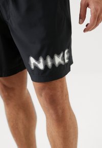 Pantaloni da nuoto neri realizzati in materiale leggero, con un design grafico bianco ondulato sul lato inferiore e tasche laterali.