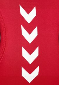 Röd idrottsstoff med en slät textur har tre vita chevronmönster som är arrangerade vertikalt. Designen är enkel och symmetrisk.