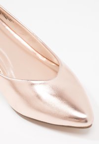 Ballerines en rose doré métallisé avec un bout pointu, une texture lisse et un profil bas. L'intérieur présente une semelle de couleur claire.