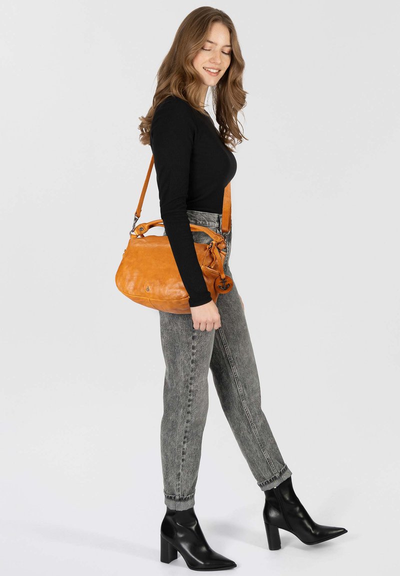 Oranje leren handtas met een gebogen vorm, afneembare schouderriem en zilveren hardware; gecombineerd met grijze high-waisted jeans en zwarte hakschoenen.