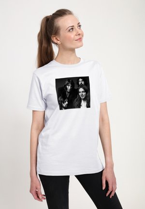 Ung kvinde med hestehale bærer en hvid T-shirt med sort-hvidt foto af fire mænd med langt hår og skæg.
