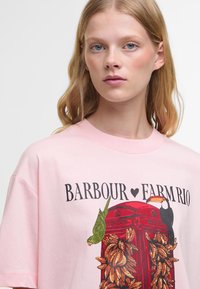 Ροζ βαμβακερό μπλουζάκι με γραφικό σχέδιο ενός κόκκινου τηλεφωνικού θαλάμου διακοσμημένου με πράσινους παπαγάλους και μπανάνες. Στρογγυλή λαιμόκοψη, χαλαρή εφαρμογή.