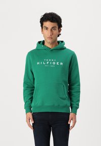 Hanorac verde din amestec de bumbac, cu un buzunar tip kangur pe față. Prezintă un text cu logo alb "TOMMY HILFIGER EST. 1985" pe piept.