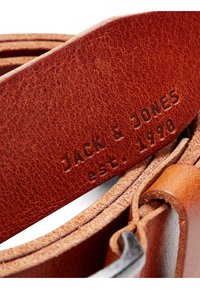Brun læderbælte med en struktureret overflade. Spændet er af sølvfarvet metal og har det præget brandnavn "JACK & JONES" samt "est. 1990."