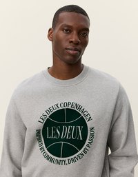 Γκρι φούτερ με στρογγυλή σκούρα πράσινη γραφική απεικόνιση που περιλαμβάνει "Les Deux Copenhagen" και κείμενο σε λευκό. Ριγέ λαιμόκοψη και μανίκια.